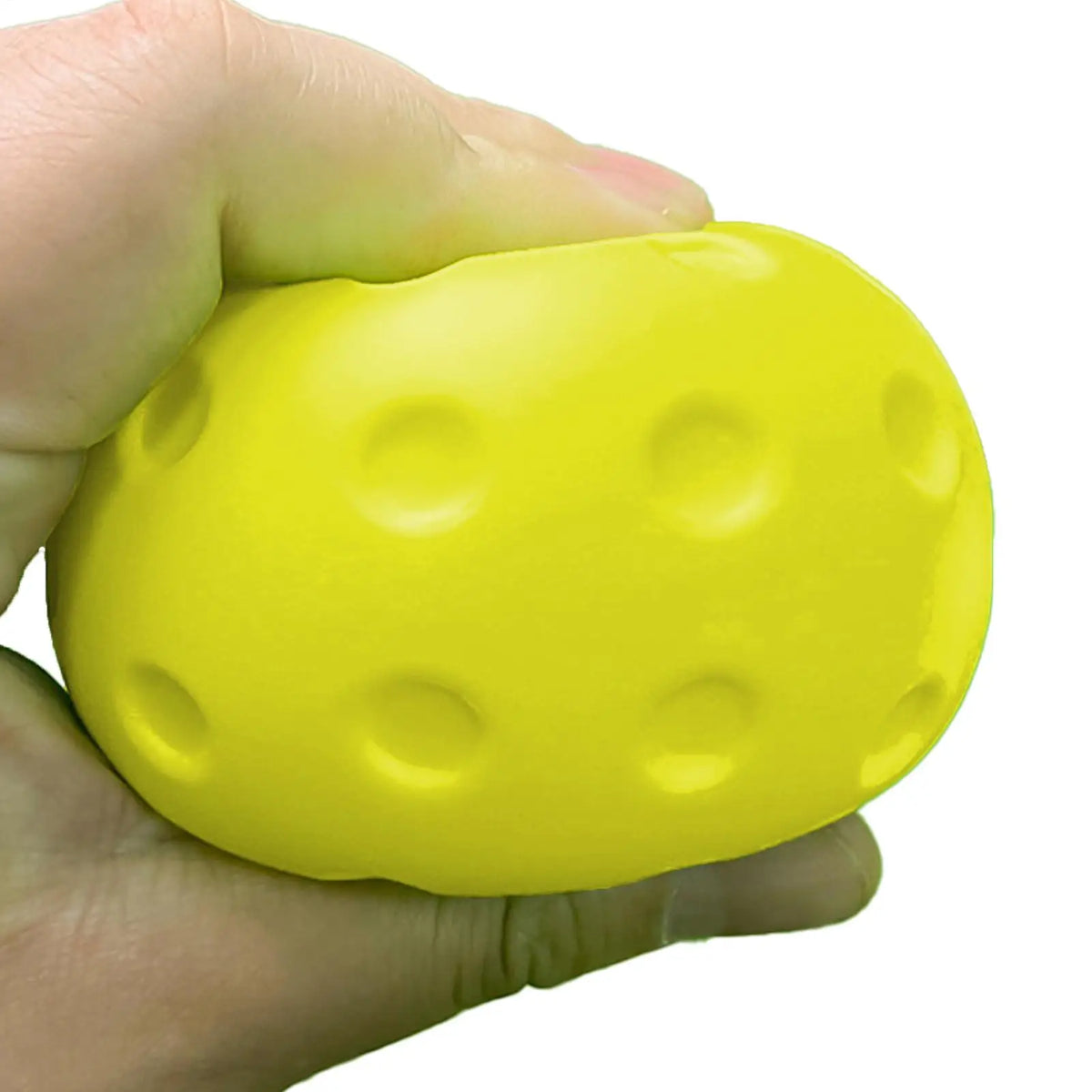Balle de pickleball en mousse jaune écrasée dans une main pour montrer sa texture souple et silencieuse