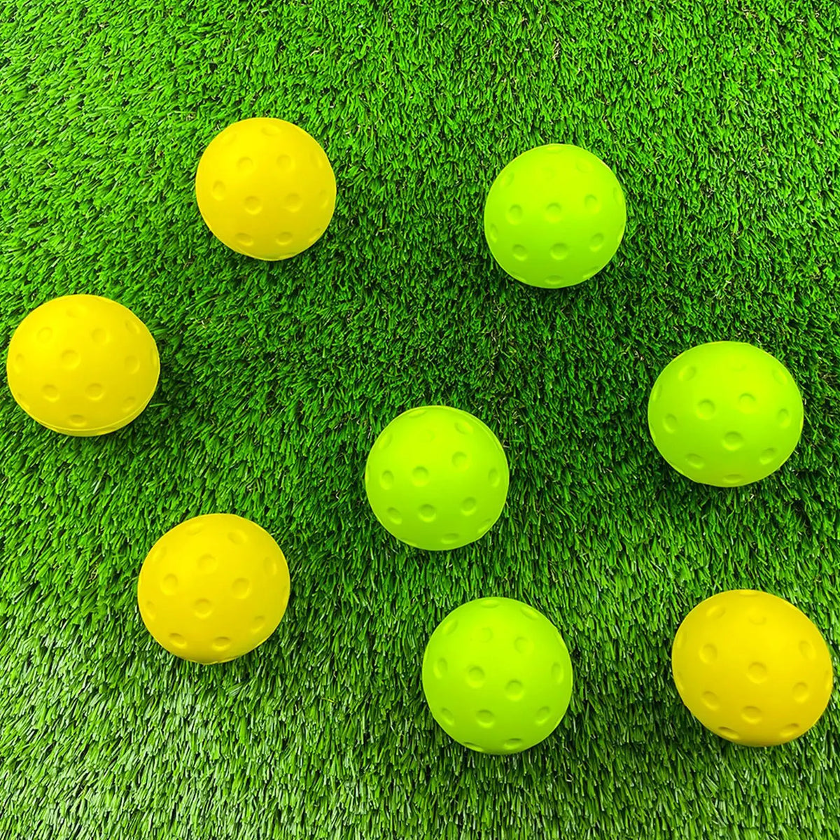Balles de pickleball en mousse jaunes et vert citron posées sur un gazon synthétique, huit balles dispersées