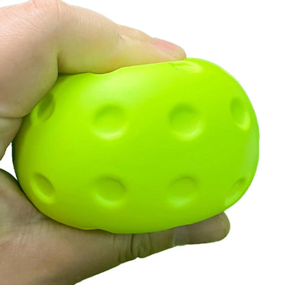 Balle de pickleball en mousse vert citron pressée entre les doigts, montrant sa souplesse et ses alvéoles