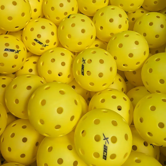 Balles de pickleball X-ace extérieur jaunes vues du dessus, des dizaines de balles perforées entassées