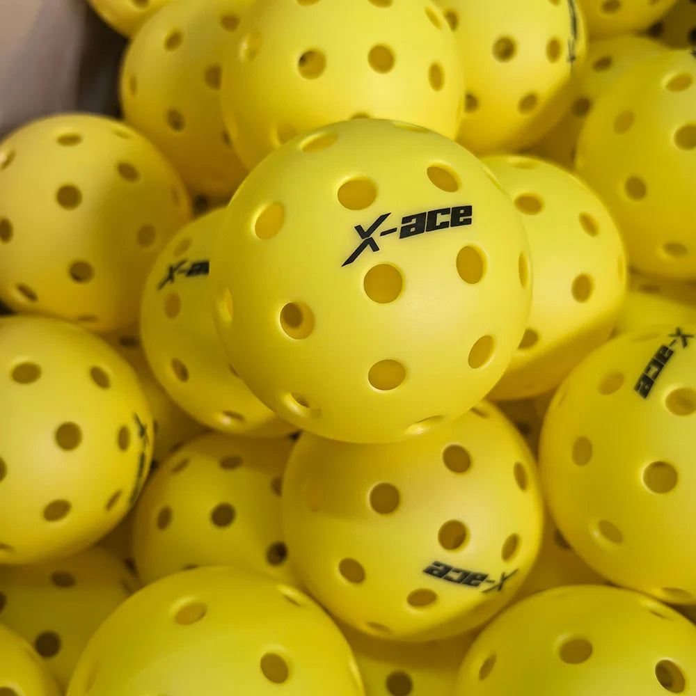 Balles de pickleball X-ace jaunes à 40 trous en vrac, gros plan sur une balle portant le logo noir de la marque